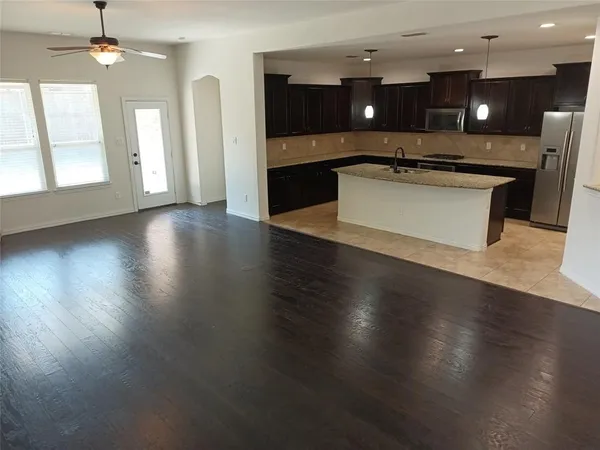 an open kitchen with a refrigerator a sink dishwasher a stove and a dining table with wooden floor