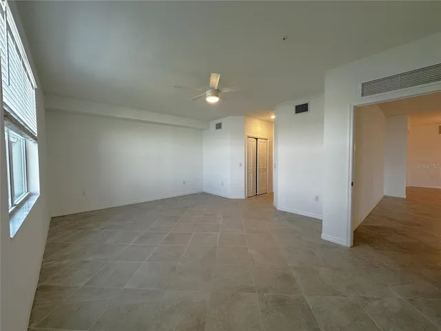 an empty room with chandelier fan and windows