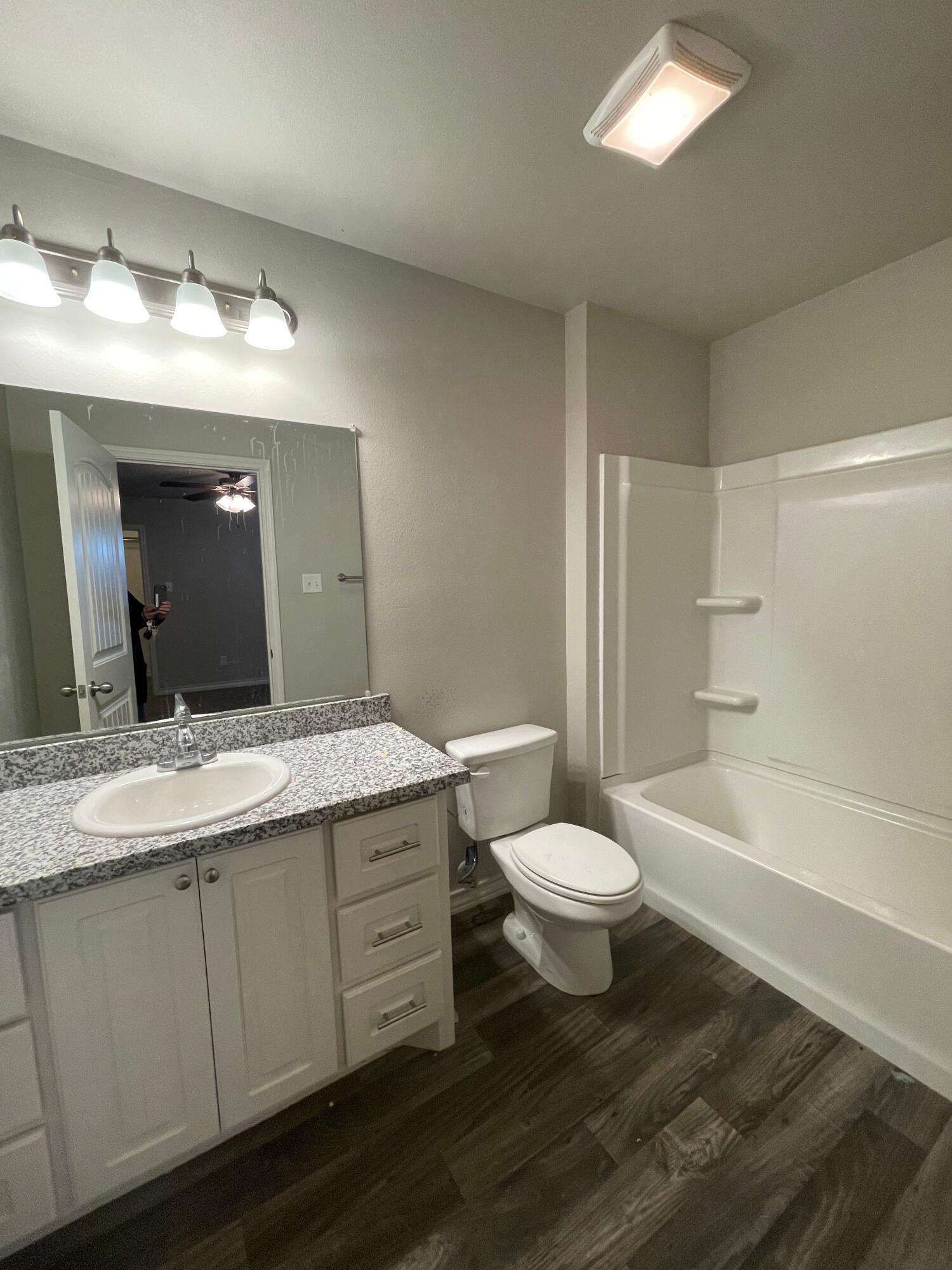 6040 24th Street, Unit 29 Lubbock, TX 79407 - Photo 9 of 15 a bathroom with a granite countertop sink toilet a large mirror and a tub