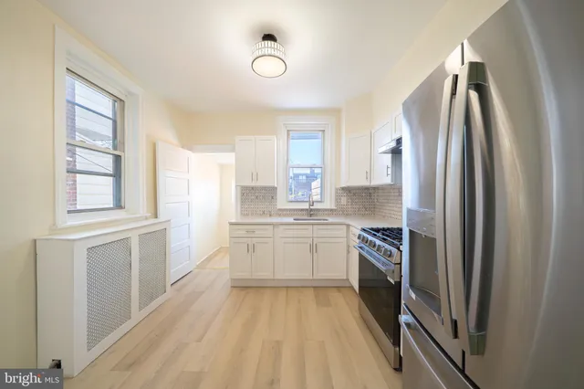 a large kitchen with a refrigerator a sink dishwasher a stove and white cabinets with wooden floor