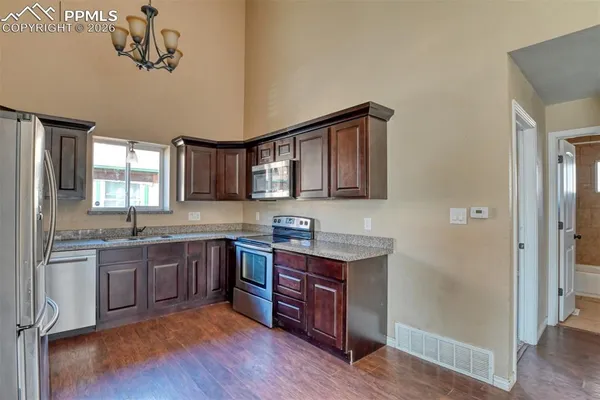 a kitchen with stainless steel appliances granite countertop wooden cabinets a sink a stove a dining table and chairs
