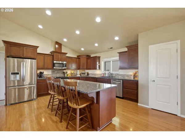 a kitchen with stainless steel appliances kitchen island granite countertop a refrigerator a stove a sink dishwasher and a dining table with wooden floor