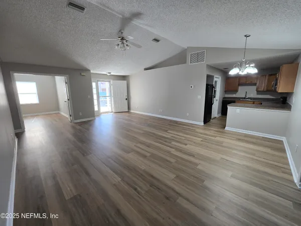 an empty room with wooden floor chandelier and windows