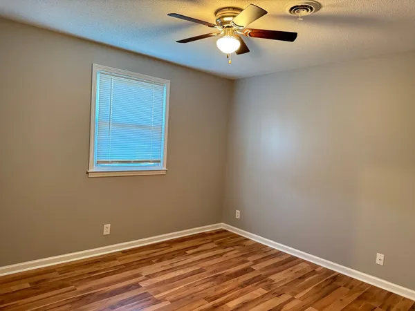 a view of an empty room with wooden floor and a ceiling fan