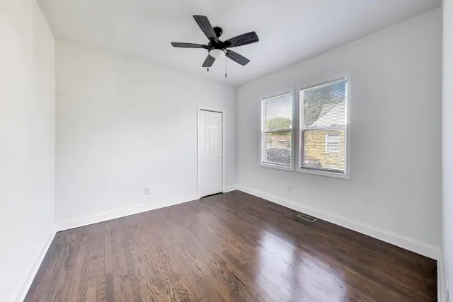 an empty room with wooden floor ceiling fan and windows