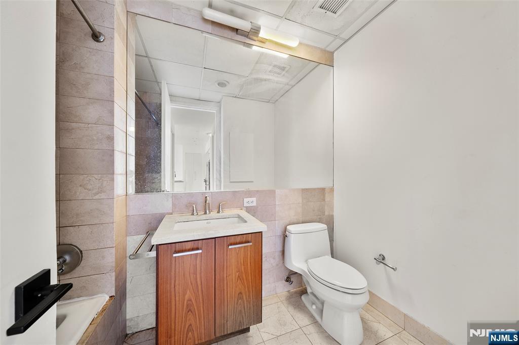 4 Beacon Way, Unit 1407 Jersey City, NJ 07304 - Photo 13 of 19 a bathroom with a granite countertop toilet sink and mirror