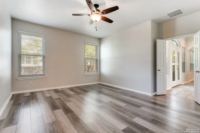 an empty room with wooden floor fan and windows