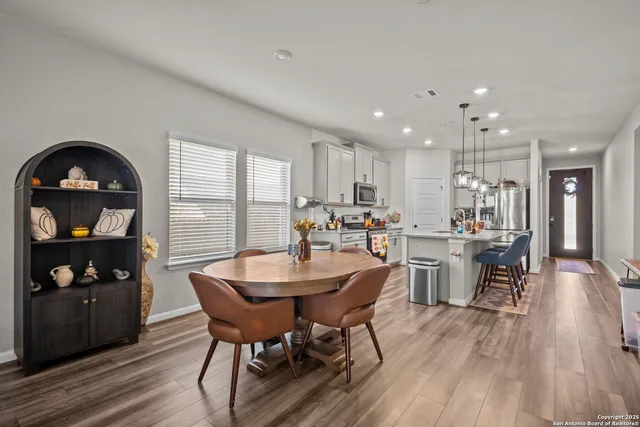 a kitchen with stainless steel appliances granite countertop a stove a refrigerator a kitchen island a sink cabinets and a dining table with wooden floor