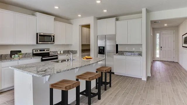 a kitchen with granite countertop a stove a sink a microwave a refrigerator and white cabinets with wooden floor