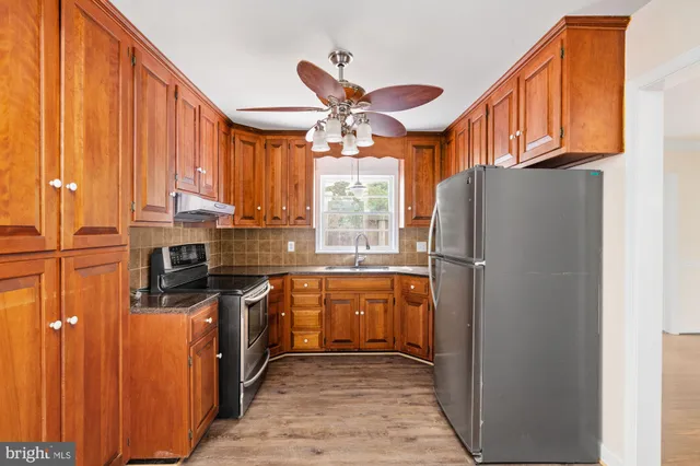 a kitchen with stainless steel appliances granite countertop a refrigerator a sink dishwasher a stove and a dining table with wooden floor