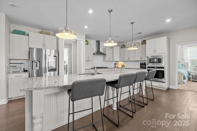 a kitchen with stainless steel appliances kitchen island granite countertop a refrigerator a stove a kitchen island and chairs with wooden floor