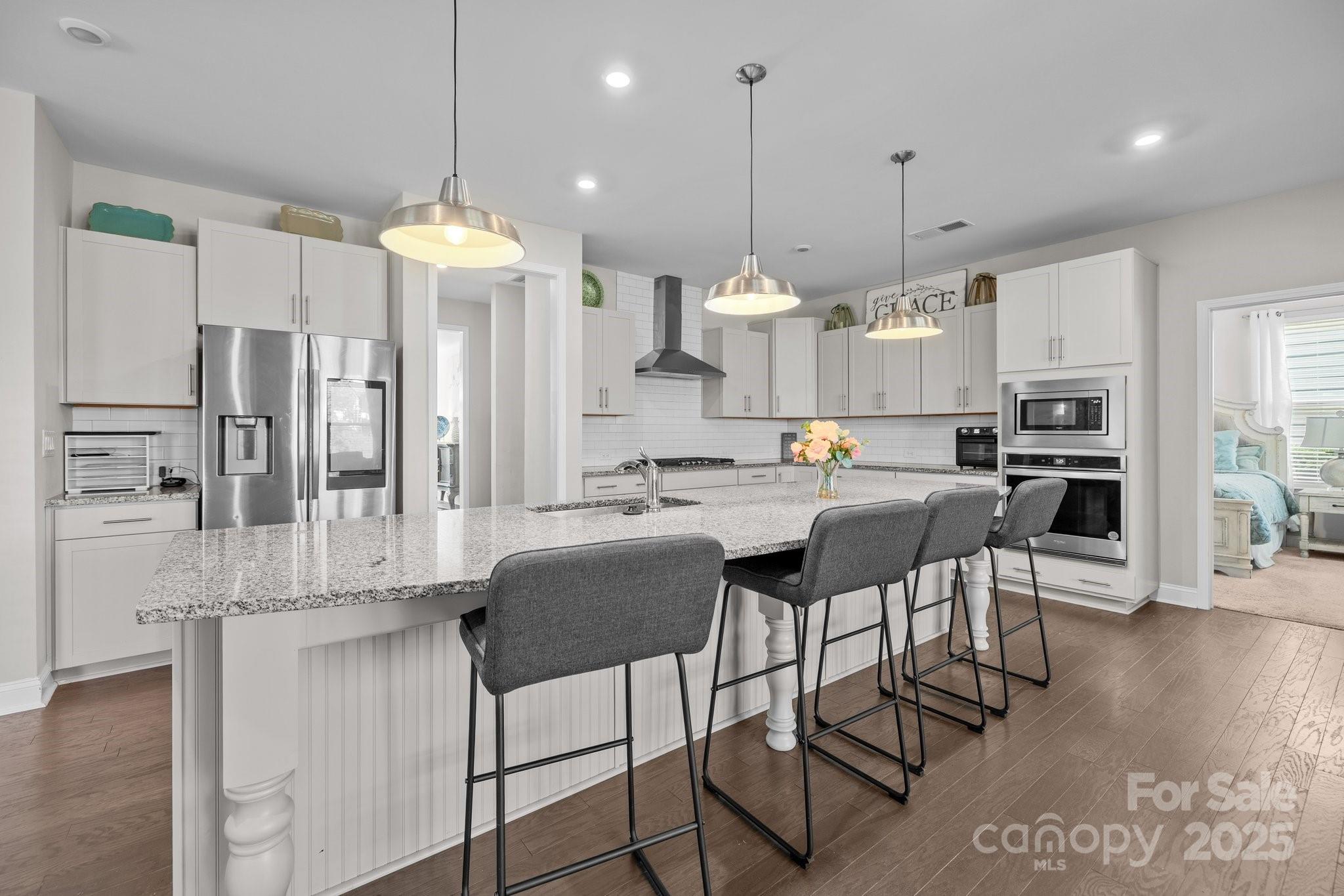 a kitchen with stainless steel appliances kitchen island granite countertop a refrigerator a stove a kitchen island and chairs with wooden floor
