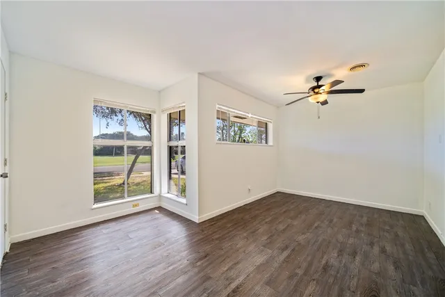 an empty room with wooden floor ceiling fan and windows