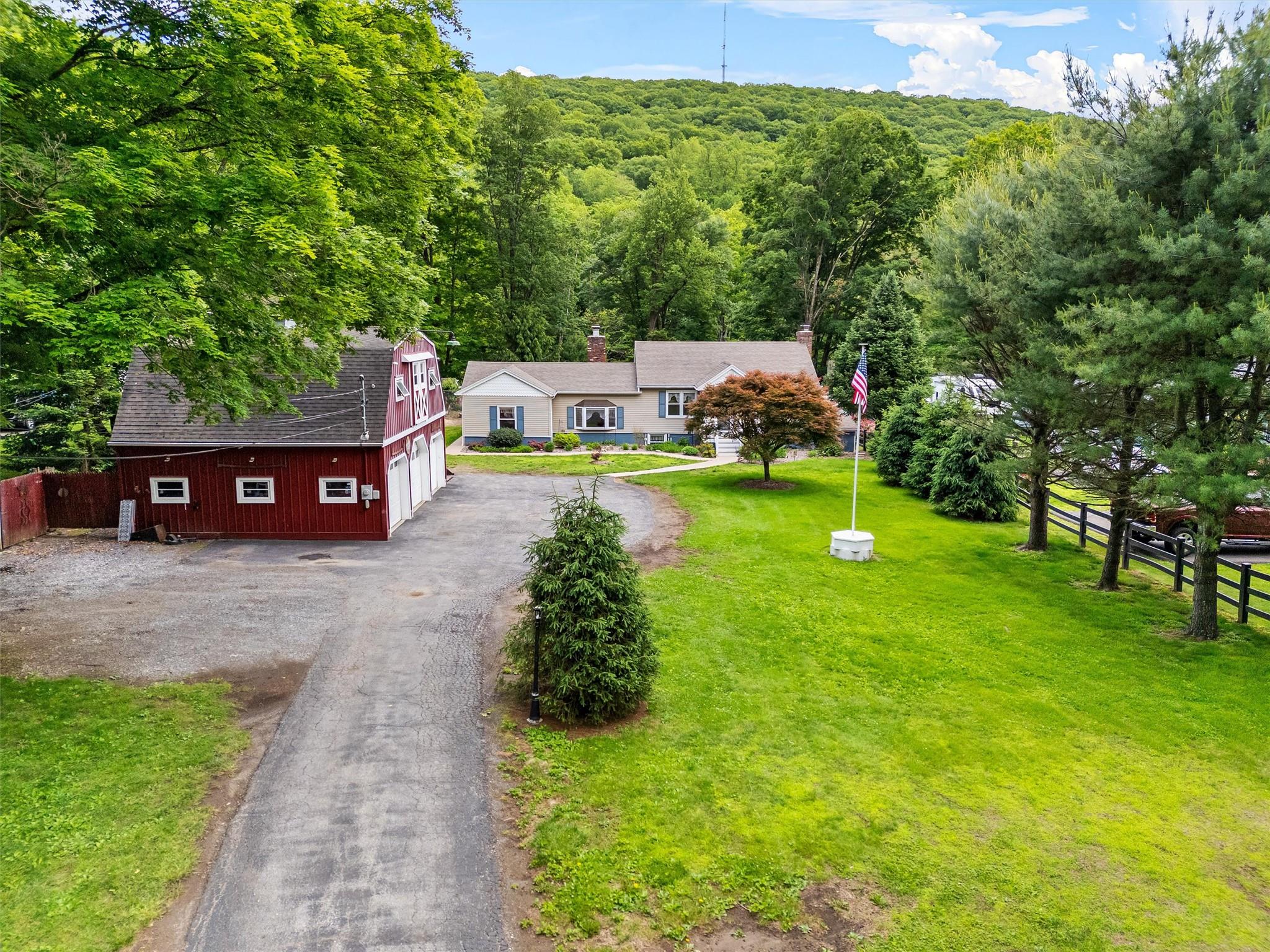 View of front of home featuring a shingled roof, an outbuilding, a wooded view, driveway, and a barn