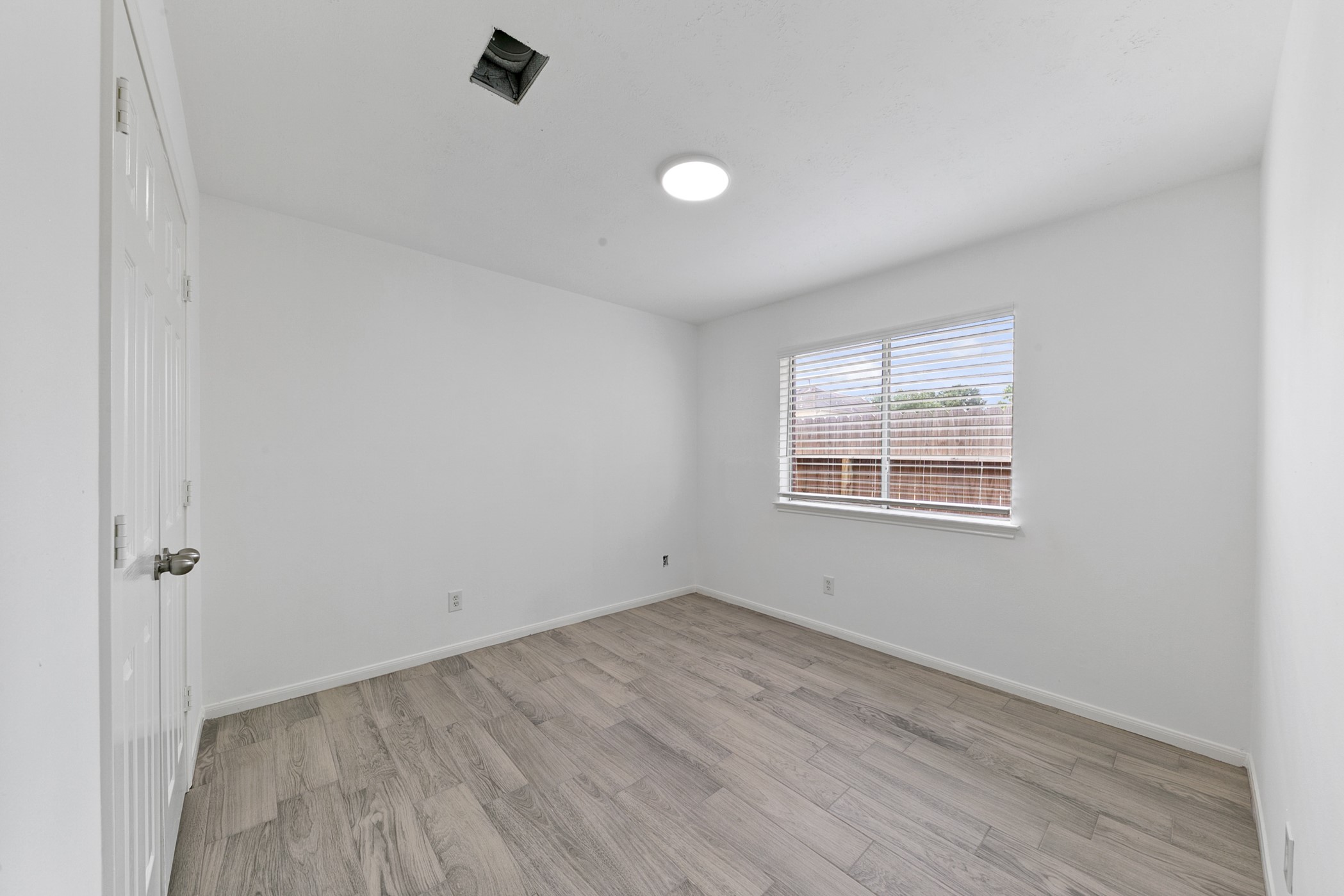 12014 Raven View Drive Houston, TX 77067 - Photo 8 of 29 This is a bright, empty room with light wood flooring, white walls, and a window with blinds allowing natural light. There's a white door on the left and a ceiling light fixture.