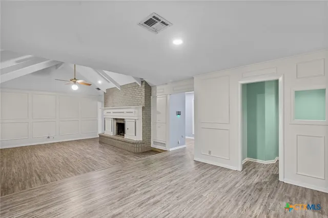 an empty room with wooden floor fireplace and windows