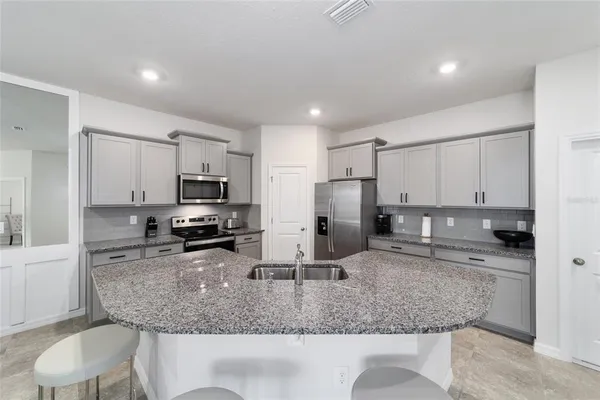 a kitchen with stainless steel appliances granite countertop a sink a microwave a refrigerator and a counter top space
