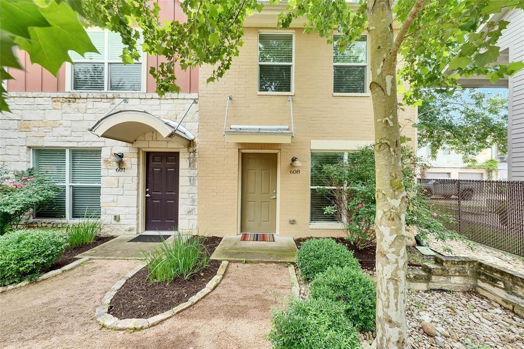 a view of a brick house with large windows plants and large tree