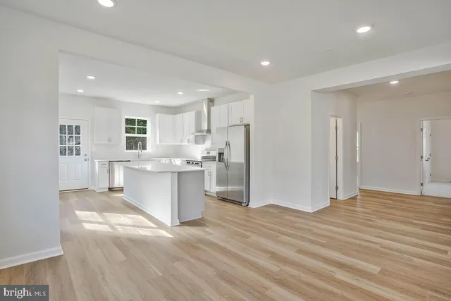 a view of a kitchen with kitchen island white cabinets wooden floor and stainless steel appliances