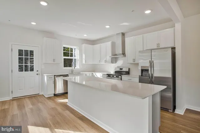 a large kitchen with kitchen island a stove a sink a refrigerator and white cabinets with wooden floor