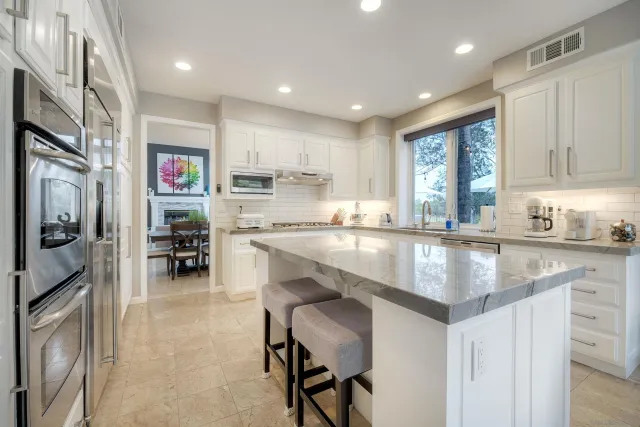 a kitchen with stainless steel appliances granite countertop a refrigerator a sink dishwasher a stove and white cabinets with wooden floor