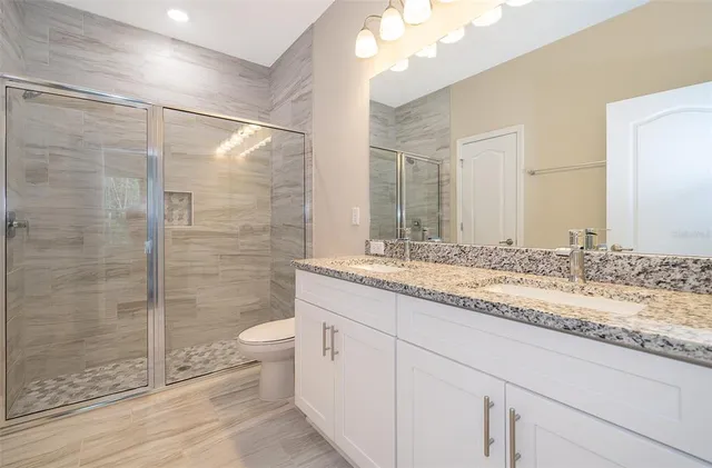 a bathroom with a granite countertop sink a toilet a mirror and shower