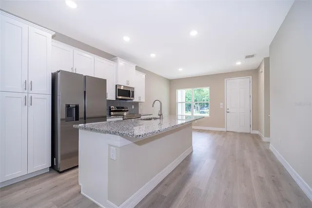 a kitchen with stainless steel appliances granite countertop a refrigerator a sink dishwasher a stove and a oven with wooden floor