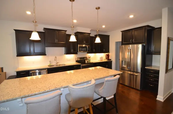 a large kitchen with stainless steel appliances kitchen island granite countertop a refrigerator a stove a sink a oven and a dining table with wooden floor