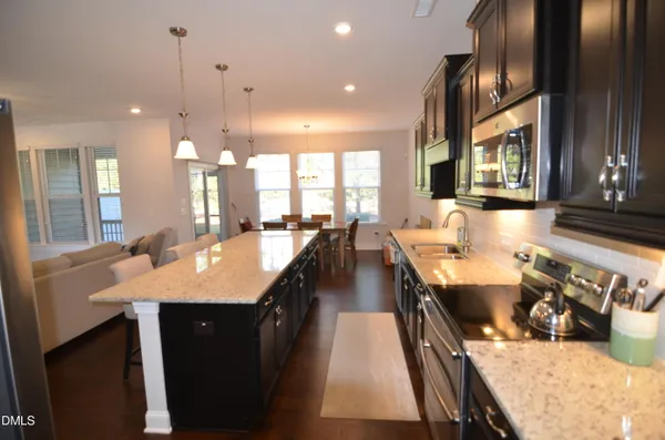 a dining hall with stainless steel appliances kitchen island granite countertop a large kitchen island a stove a sink a dining table and chairs with wooden floor