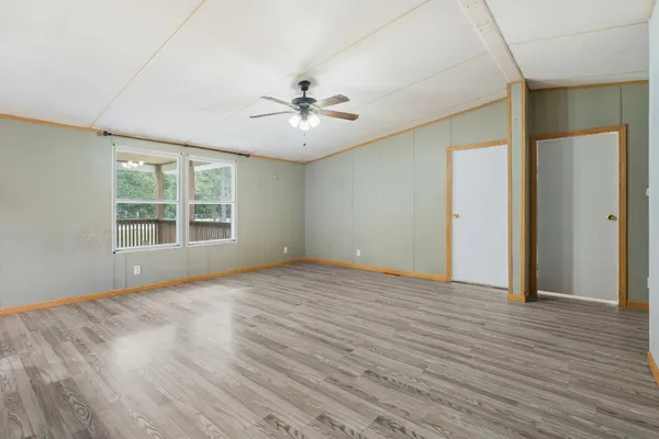 an empty room with wooden floor chandelier fan and windows