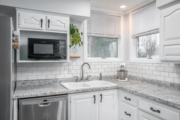 a kitchen with granite countertop a sink stainless steel appliances white cabinets and a window