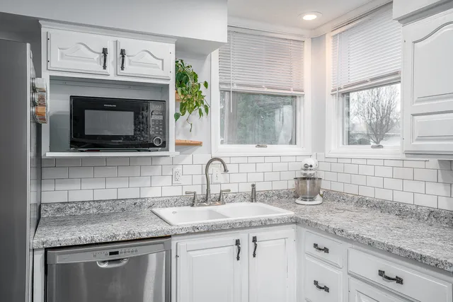a kitchen with granite countertop a sink stainless steel appliances white cabinets and a window