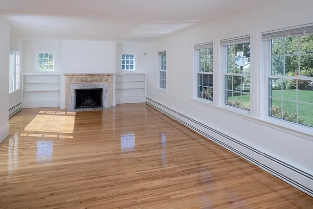 a view of a livingroom with wooden floor a fireplace and windows