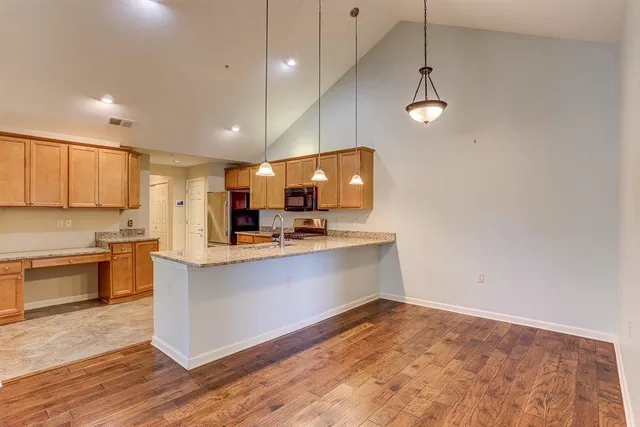 a large kitchen with stainless steel appliances a large counter top a stove a sink dishwasher a microwave oven and a dining table with wooden floor