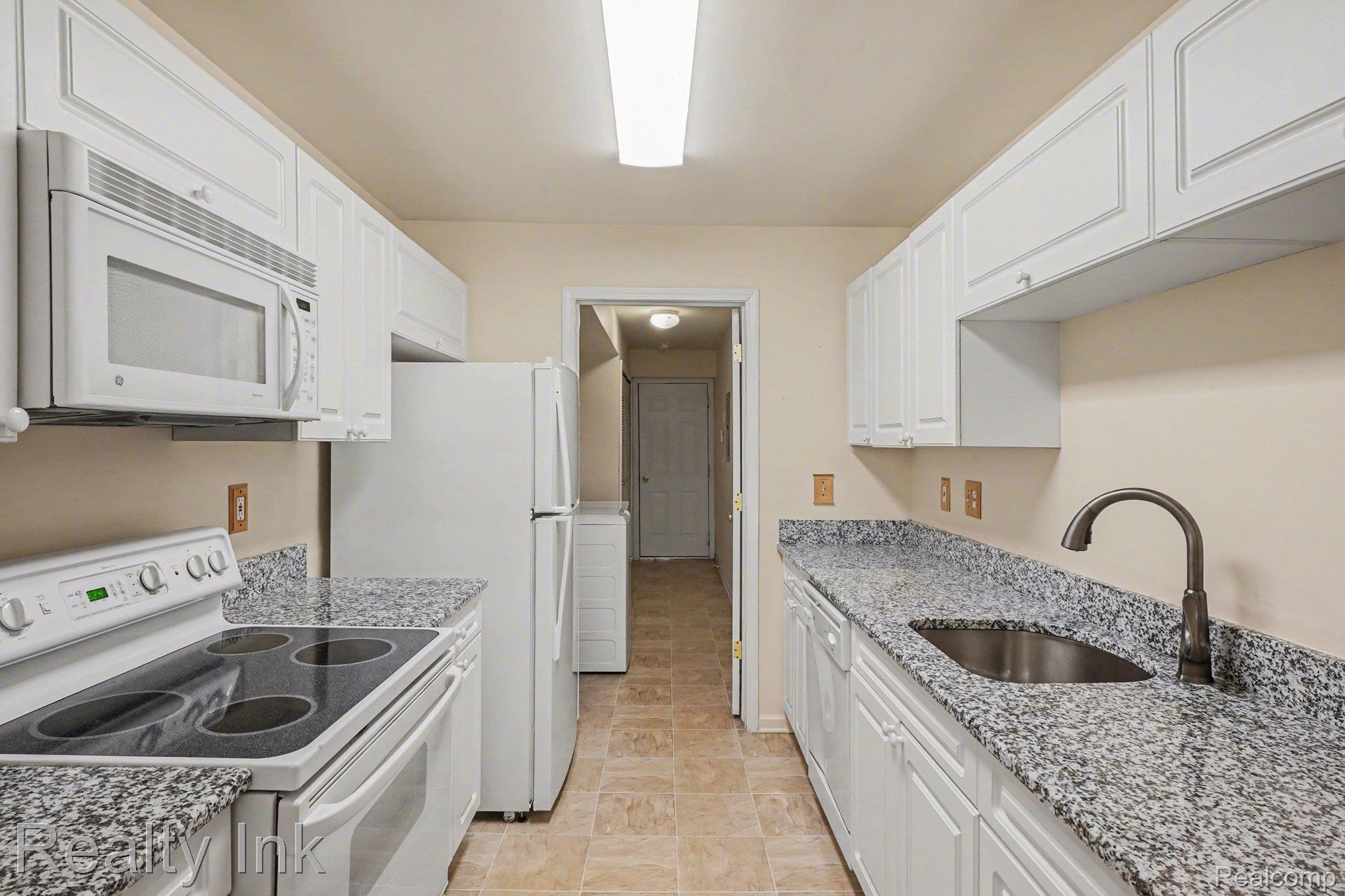 Kitchen with white appliances, white cabinets, light stone countertops, and washer / clothes dryer
