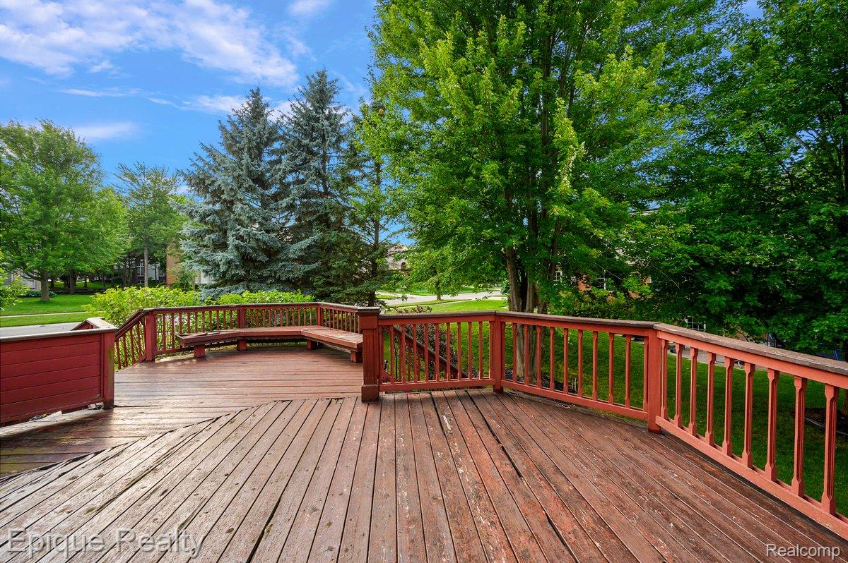 1909 Catlin Drive Rochester, MI 48306 - Photo 64 of 76 Expansive wood deck with a built-in bench seating area and red-stained railings, surrounded by mature trees and lush greenery