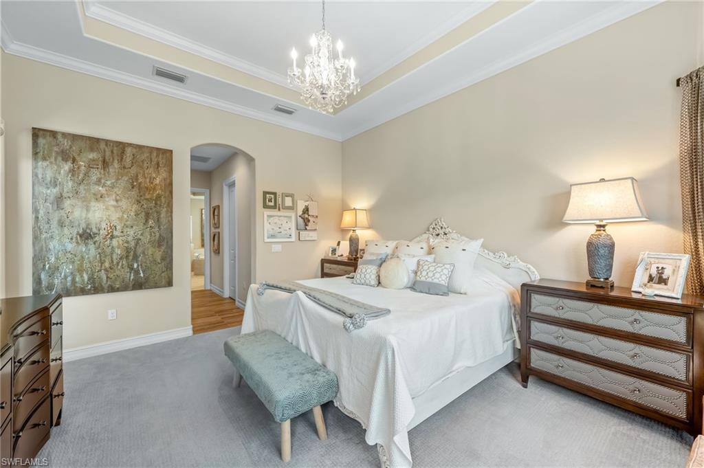 6818 Canwick Cove Circle Naples, FL 34113 - Photo 13 of 44 Bedroom with crown molding, a tray ceiling, suspended lighting, carpet floors, and ensuite bath