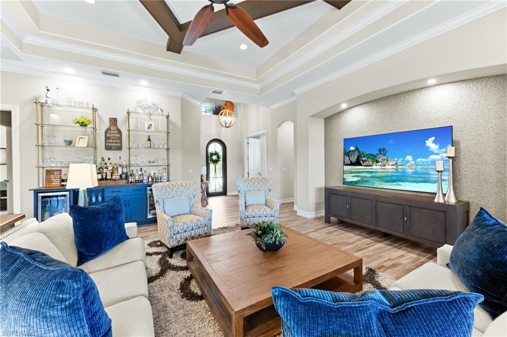 6818 Canwick Cove Circle Naples, FL 34113 - Photo 6 of 44 Living room featuring an accent wall, wood finished floors, arched walkways, bar area, and a ceiling fan