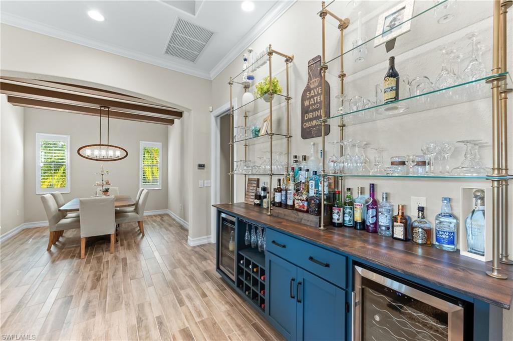 6818 Canwick Cove Circle Naples, FL 34113 - Photo 7 of 44 Bar featuring butcher block countertops, open shelves, blue cabinetry, wood finish floors, and beverage cooler