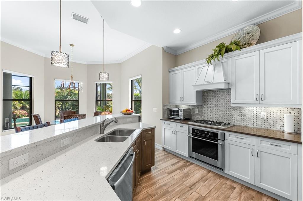 6818 Canwick Cove Circle Naples, FL 34113 - Photo 8 of 44 Two tone kitchen featuring two tone color scheme, dark stone counters, stainless steel appliances, ornamental molding, and light wood-type flooring