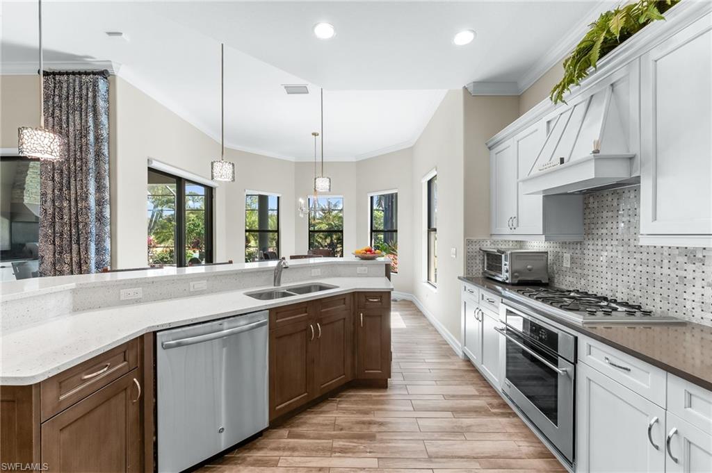 6818 Canwick Cove Circle Naples, FL 34113 - Photo 10 of 44 Dual tone kitchen featuring dual tone cabinets, ornamental molding, stainless steel appliances, decorative light fixtures, and dark stone countertops
