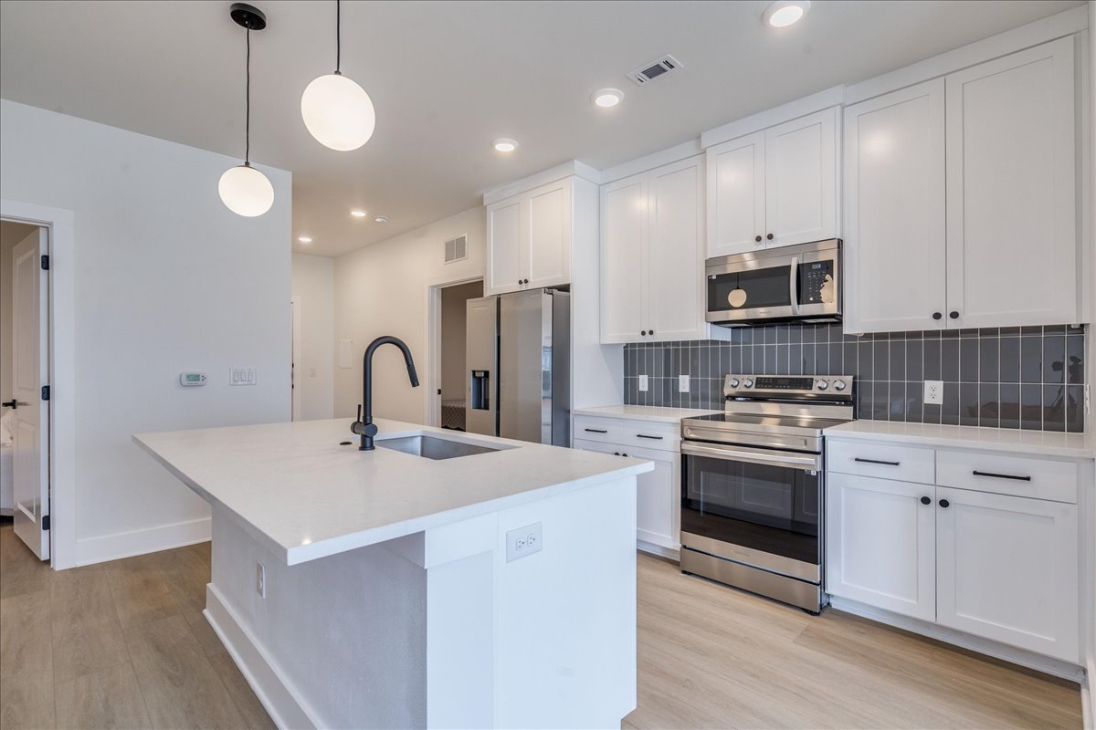 a kitchen with stainless steel appliances a sink a stove a refrigerator cabinets and a wooden floor