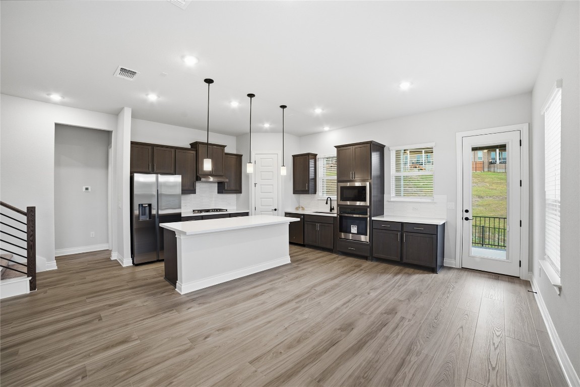 716 Coppell Court Leander, TX 78641 - Photo 6 of 40 a large kitchen with a center island wooden floor stainless steel appliances and windows