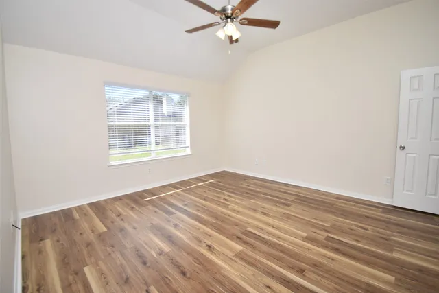 an empty room with wooden floor fan and windows