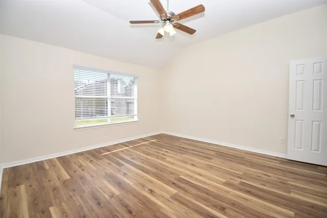 an empty room with wooden floor ceiling fan and windows