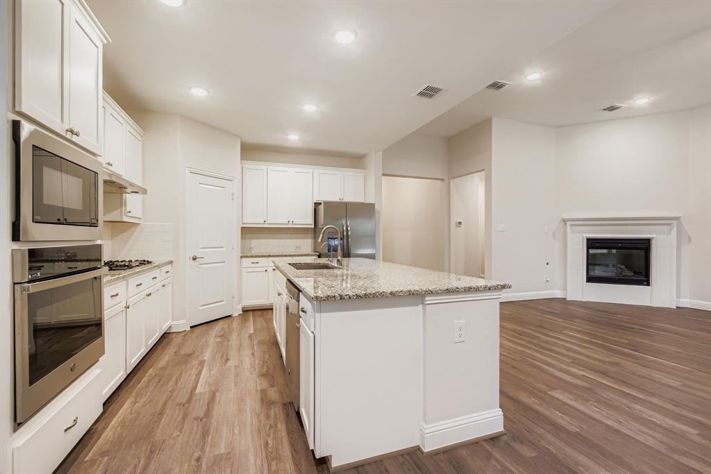 312 Magnolia Drive Oak Point, TX 75068 - Photo 9 of 28 Kitchen with appliances with stainless steel finishes, recessed lighting, light wood-style floors, light stone counters, and white cabinetry