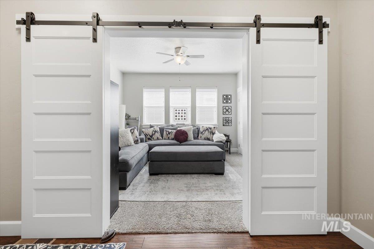 1303 West Brando Street Meridian, ID 83646 - Photo 31 of 49 Dual white barn doors with dark hardware open to a bright living area featuring wood-finish flooring, a ceiling fan with light, and multiple windows with blinds