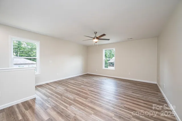 an empty room with wooden floor chandelier fan and windows
