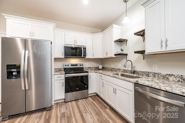 a kitchen with stainless steel appliances granite countertop a stove a sink dishwasher a refrigerator and white cabinets with wooden floor