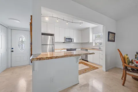 a kitchen with stainless steel appliances granite countertop a stove top oven a sink a refrigerator a dining table and chairs with wooden floor